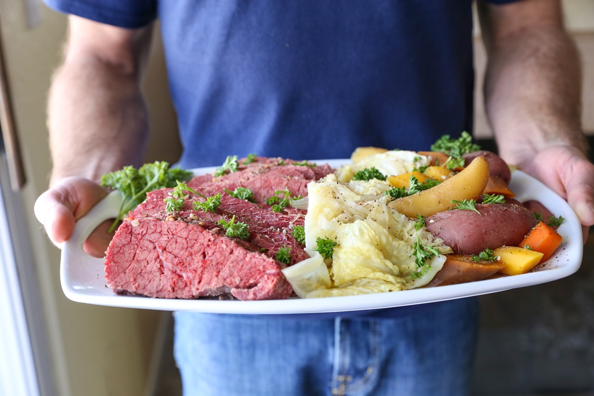 Man holding a platter of sliced corned beef, cabbage, potatoes, and carrots. Ready to serve.