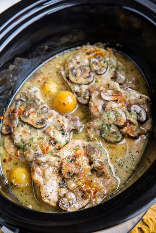 Crock pot full of pork chops covered in mushrooms, creamy sauce, onions, and potatoes.