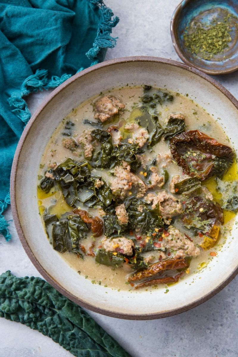 large bowl of creamy sausage and kale soup with fresh kale to the side and a spoon for eating.