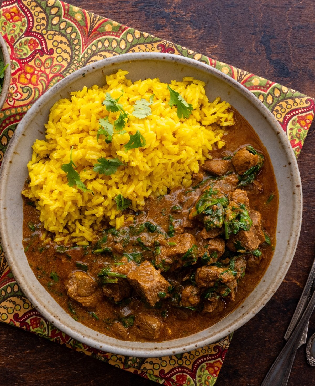 Bowl of lamb curry with saffron rice with a decorative napkin and silver forks.