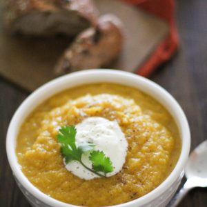 Butternut squash soup in a white bowl with yogurt and cilantro on top and a spoon to the side.