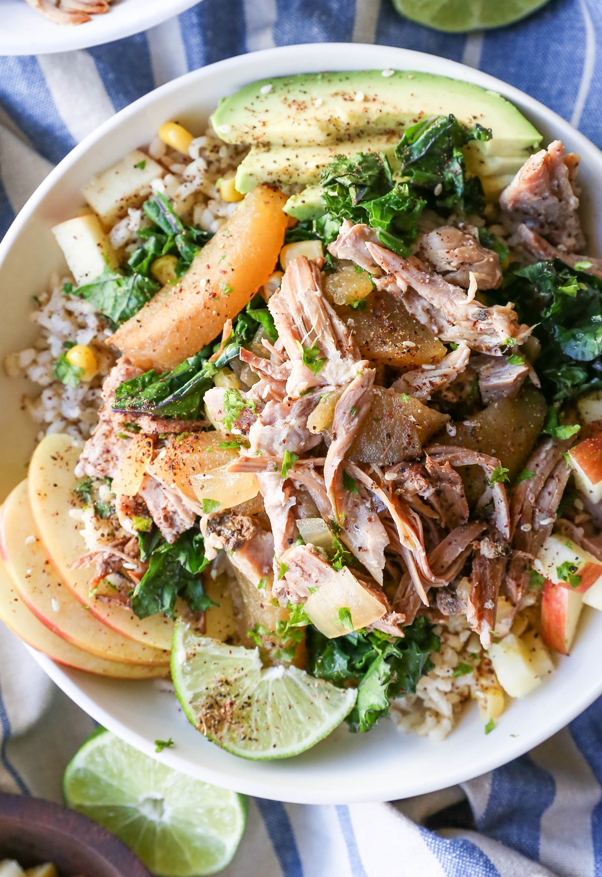 Bowl full of pulled pork, brown rice, avocado, sauteed kale and seasonings.