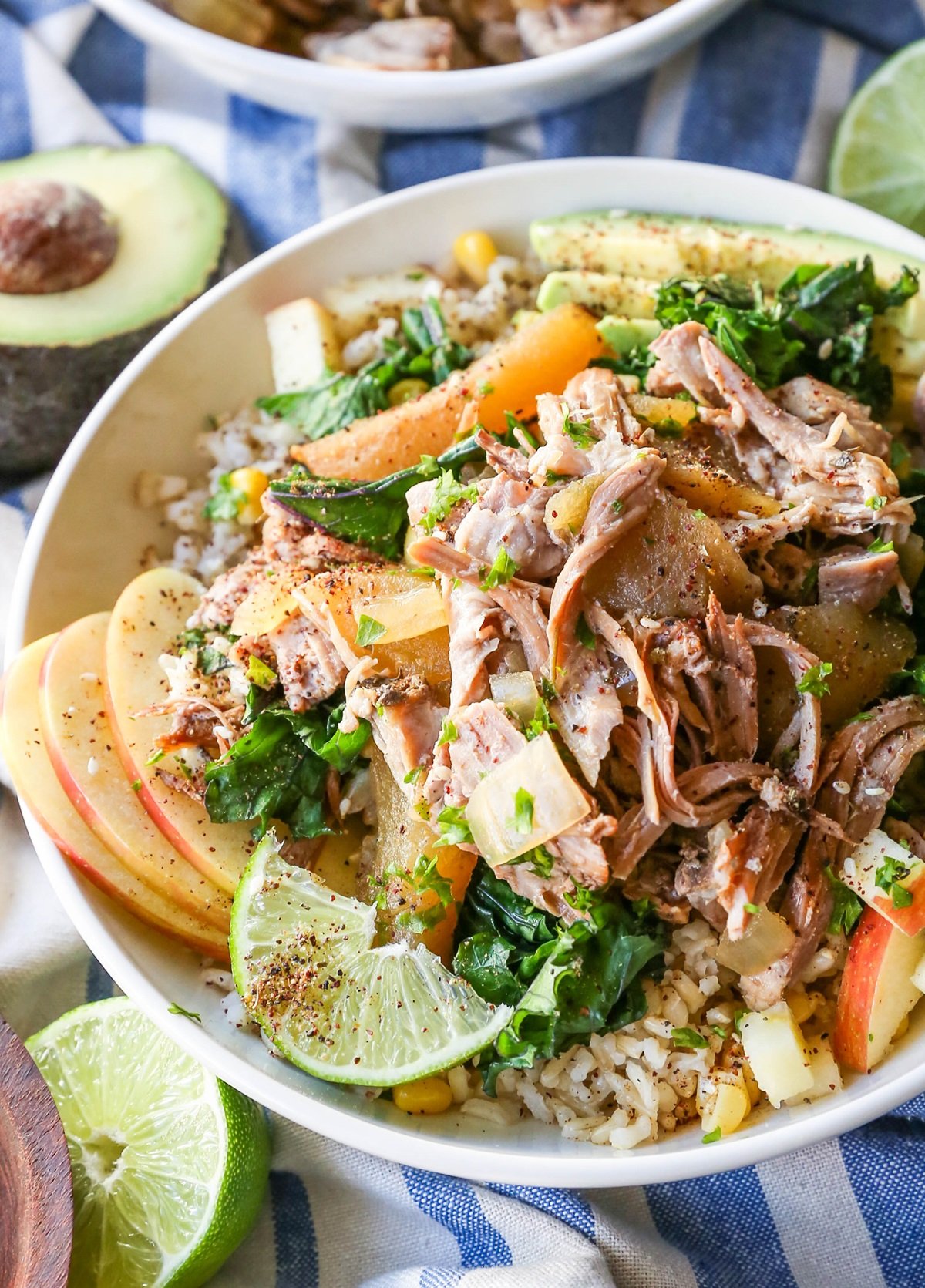 White bowl full of Crock Pot Pulled Pork, apples, brown rice, with Sauteed Kale and Avocado