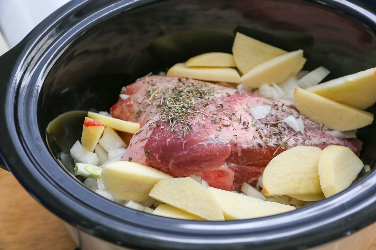 Pork shoulder roast in a crock pot with apples, onions, and garlic.
