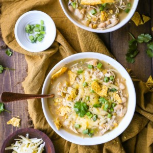 White bowls full of white chicken chili with grated cheese and green onions on top and broken corn tortilla chips