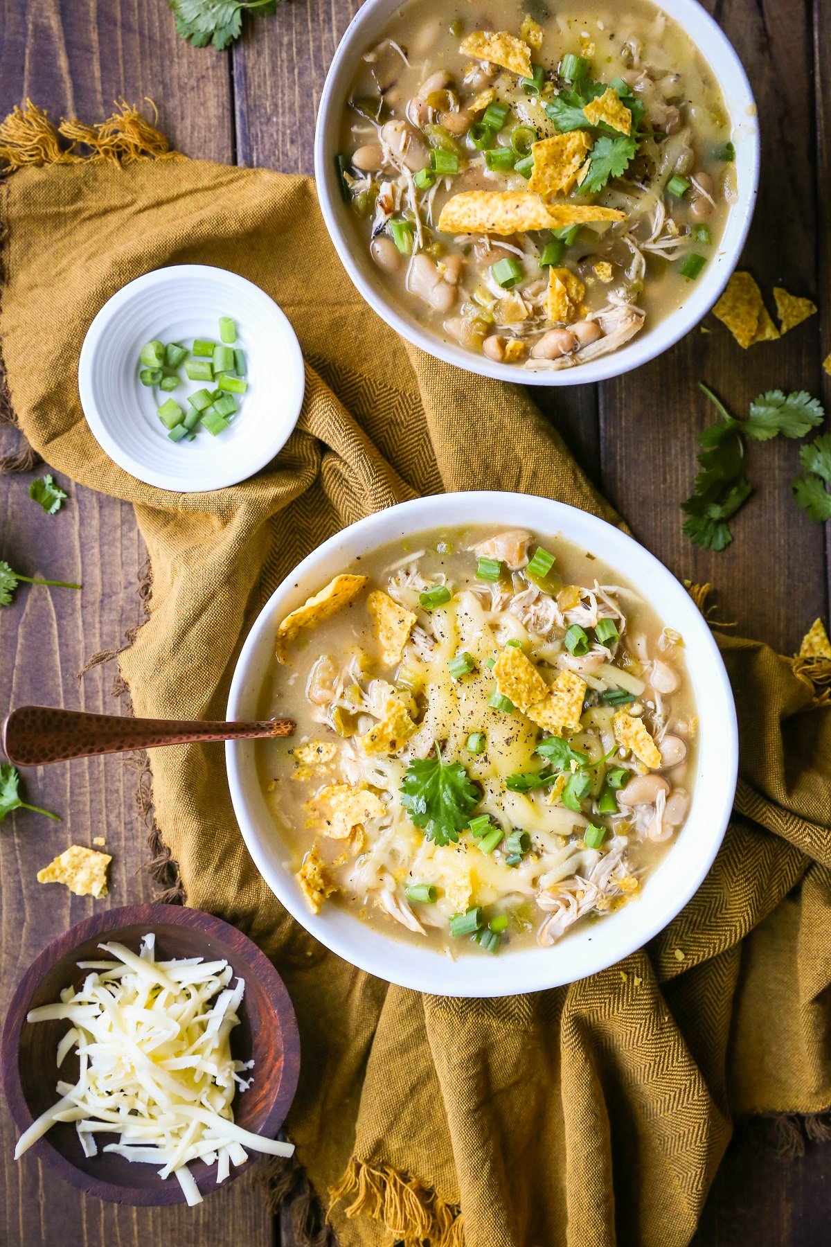 White bowls full of white chicken chili with grated cheese and green onions on top and broken corn tortilla chips