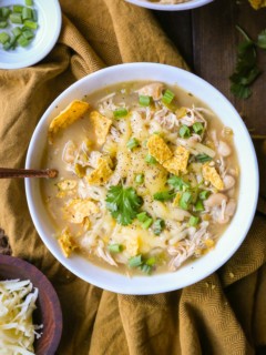 One large bowl of white chicken chili with chili toppings. A bowl of grated cheese to the side and a golden napkin.