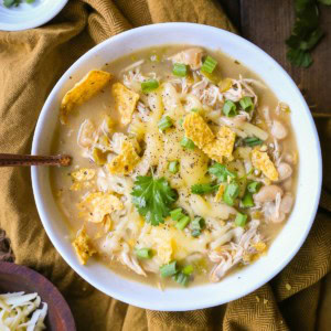 One large bowl of white chicken chili with chili toppings. A bowl of grated cheese to the side and a golden napkin.