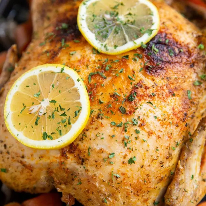 Whole chicken on a large baking sheet with veggies and sliced lemon.