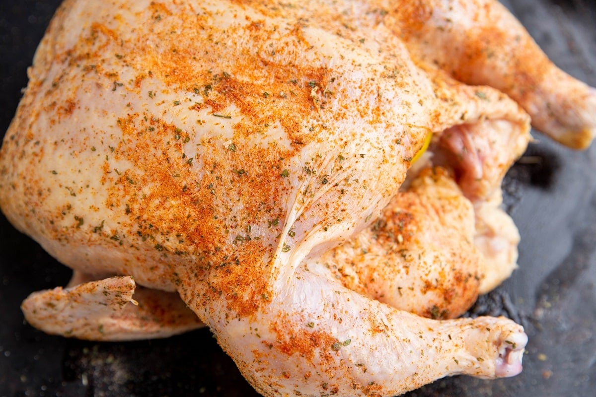 Raw whole chicken coated with oil and seasonings on a baking sheet.