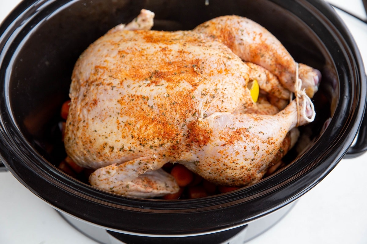 Raw whole chicken on top of vegetables in a slow cooker.