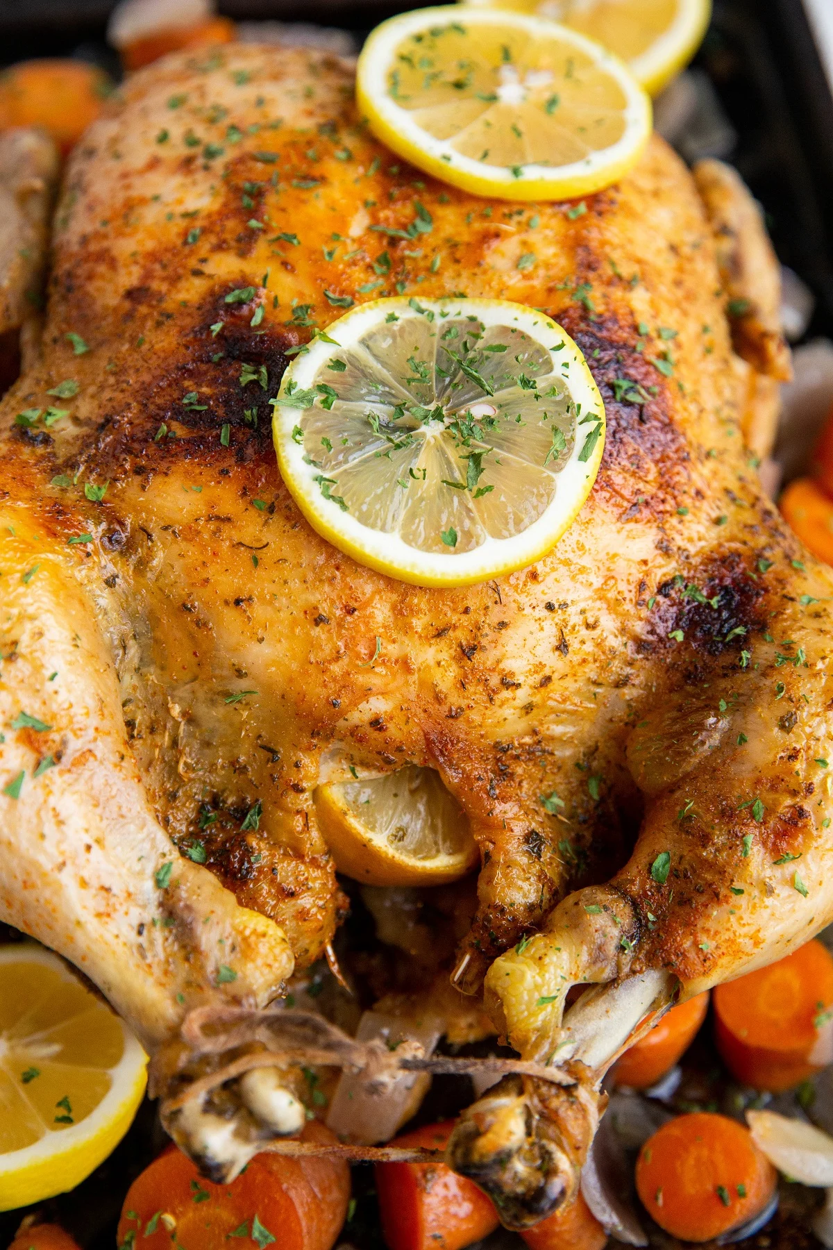 Crispy broiled chicken on a baking sheet with vegetables and lemon slices.