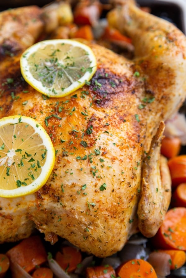 Whole cooked chicken on a baking sheet with lemon slices and vegetables.