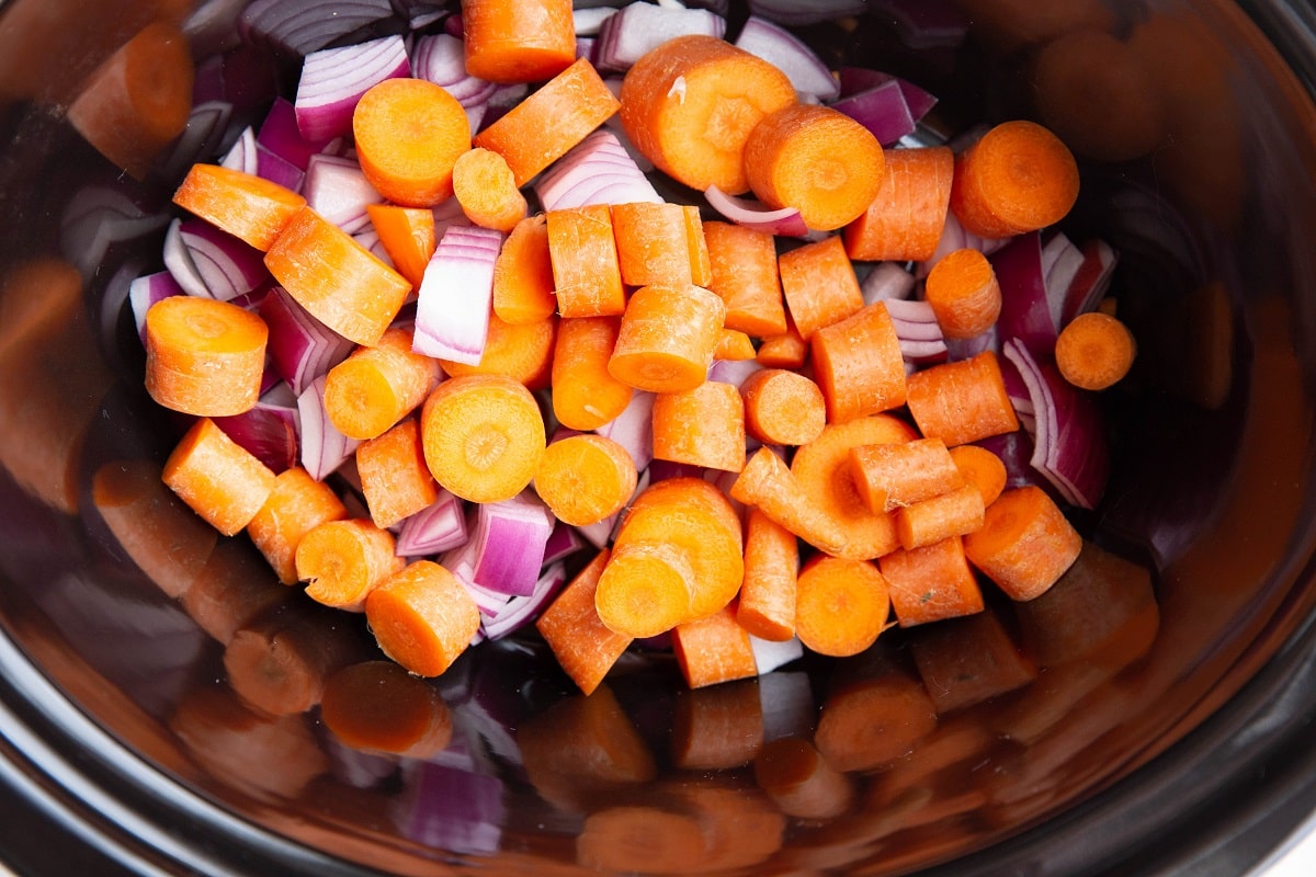 Onions and carrots at the bottom of a slow cooker.