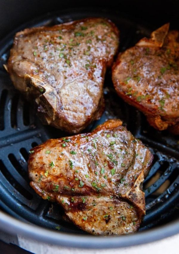 Basket of an air fryer with pork chops inside.
