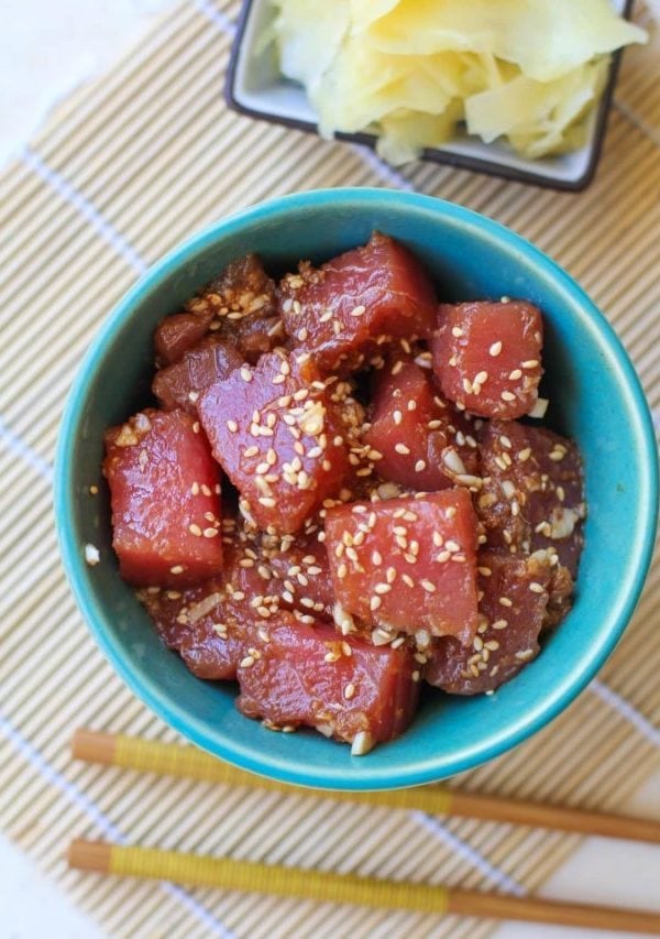 Ahi tuna poke in a teal colored bowl with chopsticks to the side and a bowl of pickled ginger. Ready to consume as an appetizer or as a main dish.