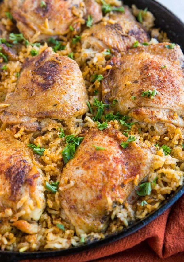 Arroz con Pollo recipe in a cast iron skillet, sprinkled with chopped fresh parsley and a red napkin to the side.