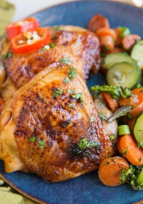Easy Baked Teriyaki Chicken Thighs on a blue plate with a green napkin with sauteed vegetables. Ready to serve.