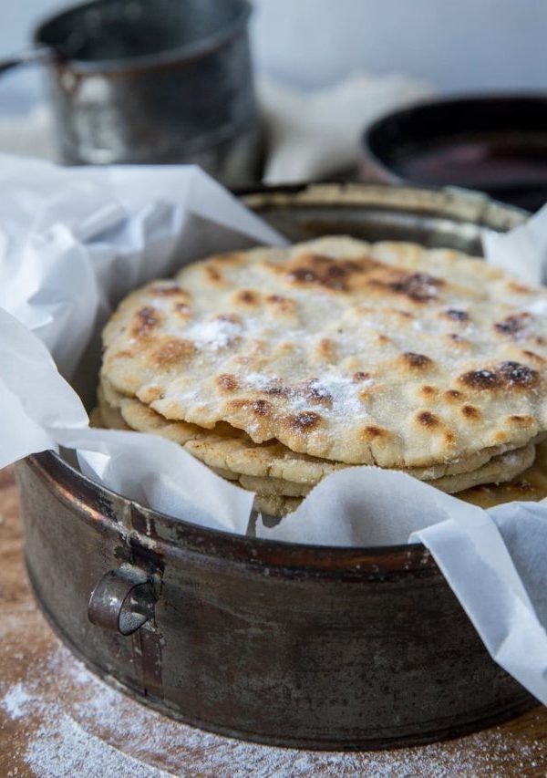 Basket of cassava flour tortillas lined in parchment paper on a wood cutting board with flour around the cutting board.