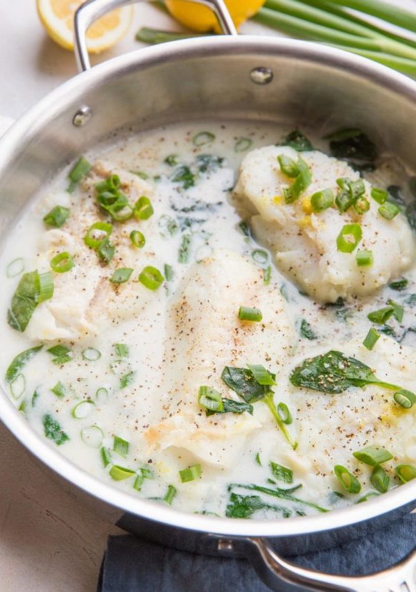 Cod fillets in a stainless steel skillet with a creamy lemon garlic sauce, sprinkled with fresh green onions.