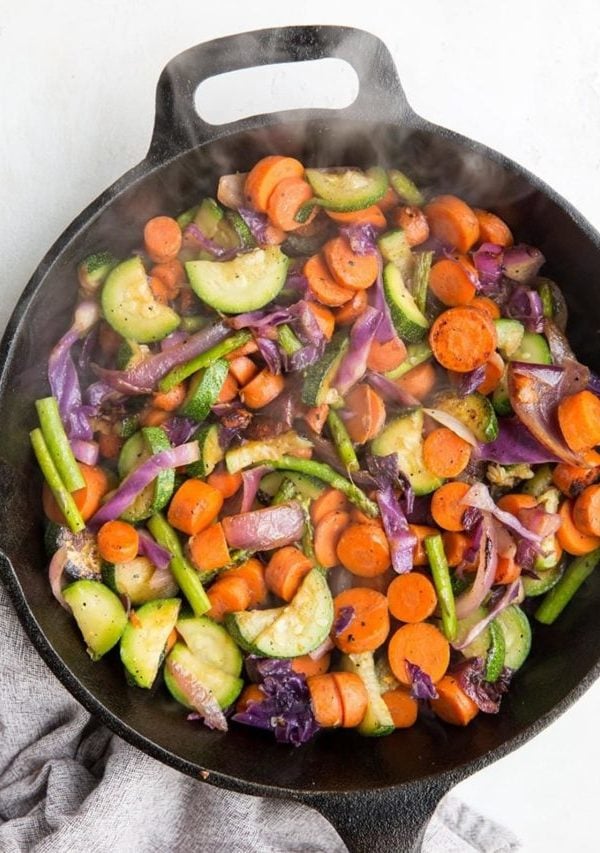Sautéed Vegetables in a cast iron skillet with steam rising up. A napkin to the side.