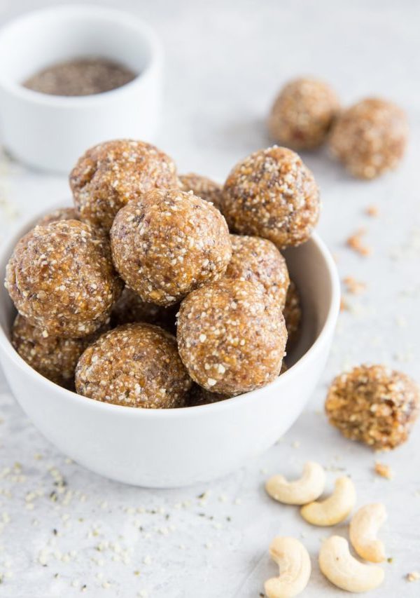 Large white bowl of energy balls with raw nuts and seeds sprinkled around, ready to eat
