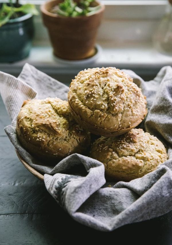basket of gluten-free hamburger buns sitting on a dark table with plants in the background.