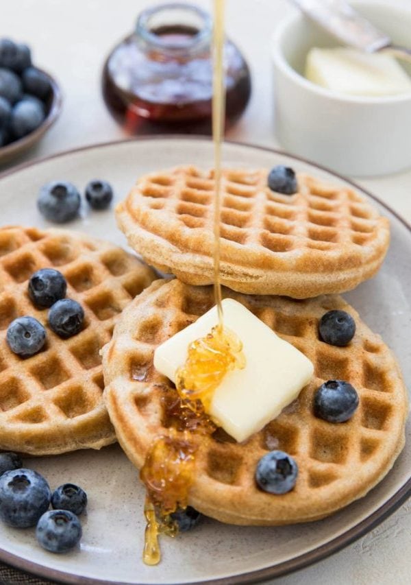 Honey pouring over waffles with butter and berries on top. Prepping to serve for breakfast.