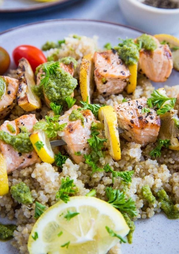 Grilled Salmon Kabobs close up with pesto sauce drizzled on top and fresh parsley sprinkled. Skewers on top of quinoa for serving.