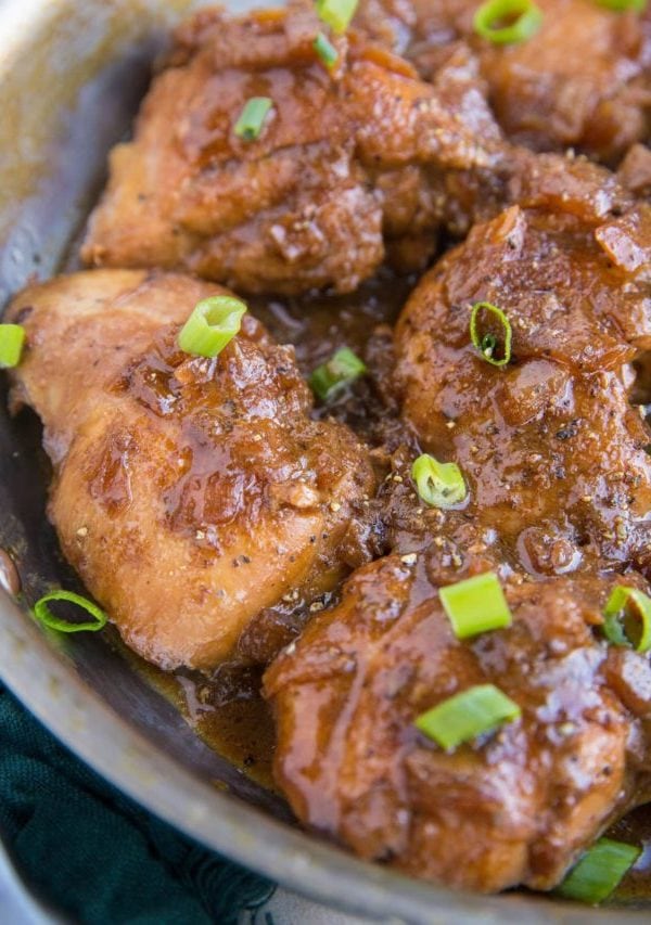 Skillet full of adobo chicken thighs, fully cooked and sprinkled with chopped green onions.