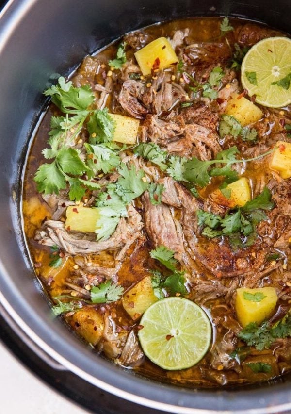 Instant pot full of shredded pork in juices with chunks of pineapple and a sprinkle of red pepper flakes and fresh cilantro. Ready to serve as a main dish.