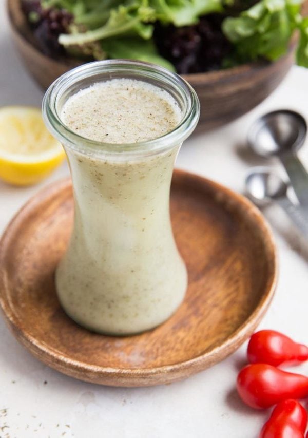 Italian salad dressing in a glass container with fresh tomatoes to the side and a salad in the background.