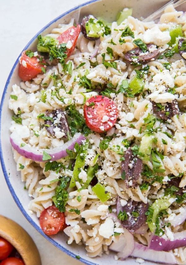 Gluten free Italian pasta salad in a large bowl with a bowl of cherry tomatoes to the side. Pasta noodles, red onions, bell peppers, cherry tomatoes, feta cheese, and more.