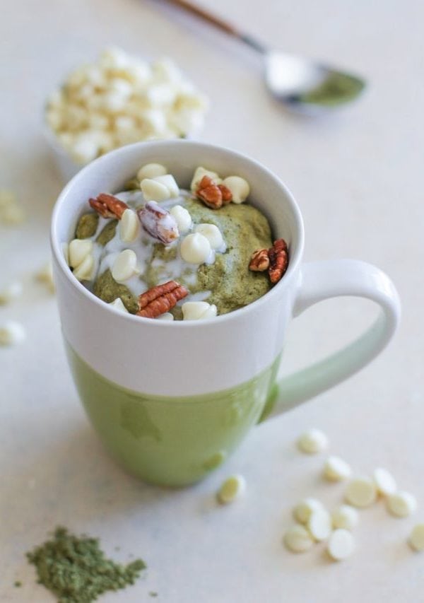 Gluten-Free and Naturally Sweetened Matcha Mug Cake in a green and white mug with white chocolate chips and matcha powder sprinkled around.