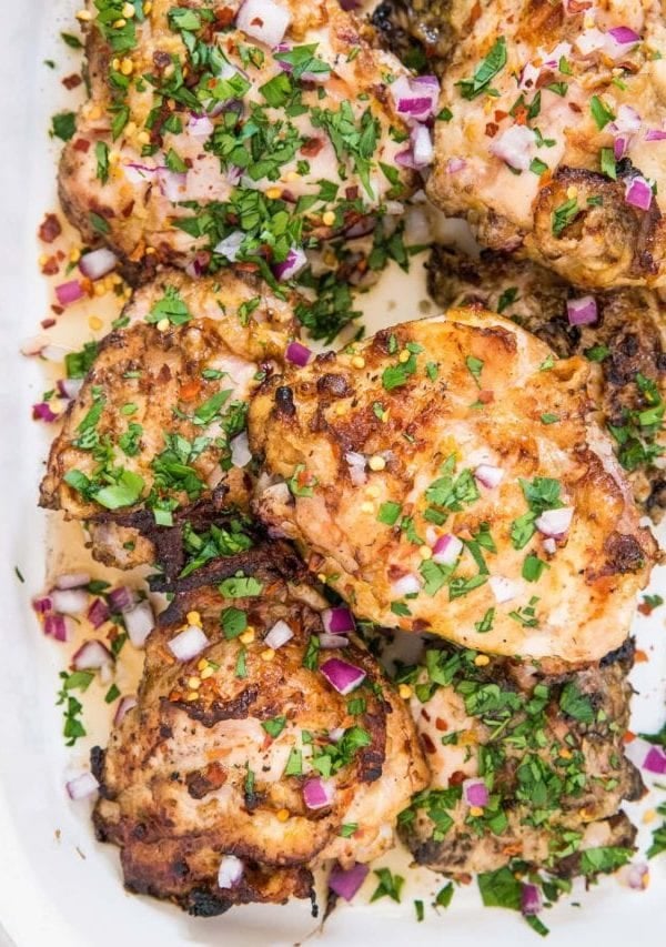 casserole dish of grilled chicken garnished with parsley and red onion