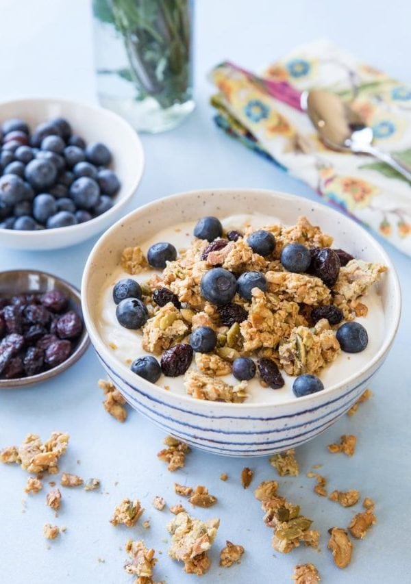 white and blue striped bowl full of yogurt with paleo granola and fresh blueberries on top. Clusters of granola all around the bowl.