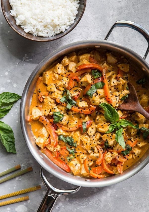 Stainless steel skillet full of chicken panang curry. A bowl of rice and chopsticks to the side.