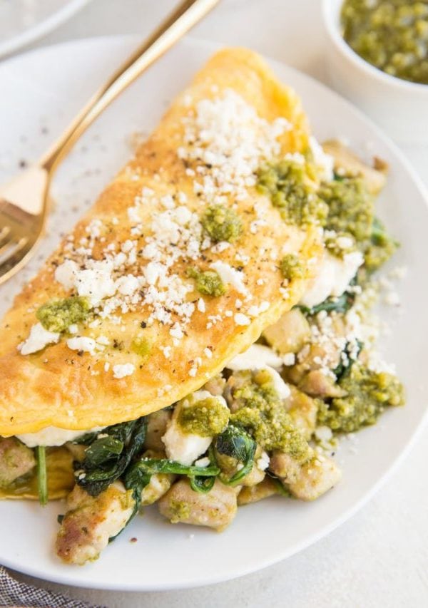 Pesto Chicken Omelette with spinach and feta on a white plate with a napkin to the side.