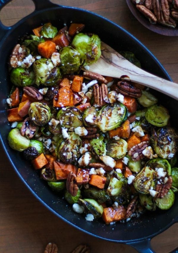 large cast iron baking dish filled with roasted brussels sprouts, sweet potatoes, pecans, feta cheese, and a balsamic drizzle. Ready to serve.