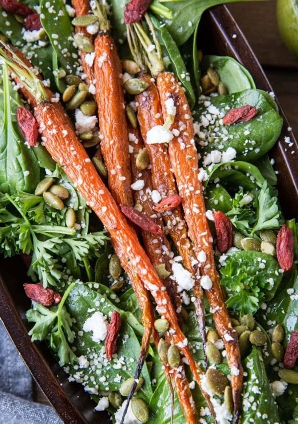 Roasted Carrot Spinach Salad with Lemon Herb Dressing in a large serving bowl. Roasted pumpkin seeds, feta cheese, and goji berries sprinkled on top