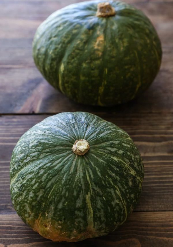 Two green kabocha squash on a wooden table.
