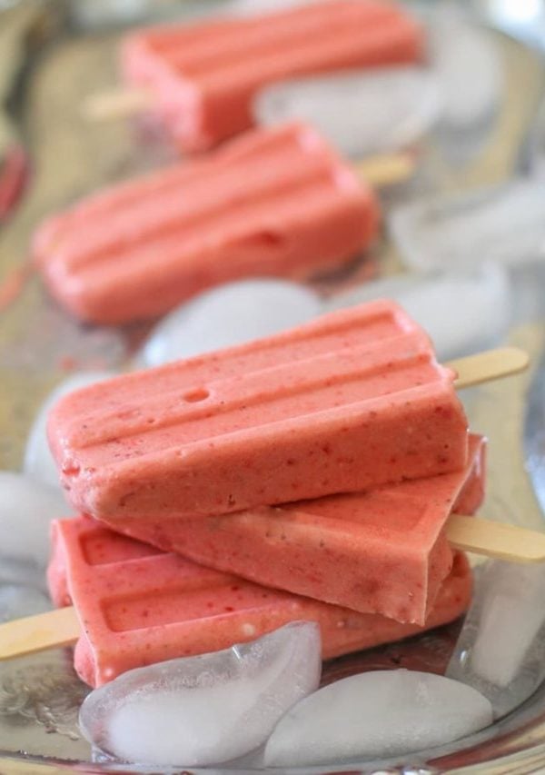Stack of strawberry coconut milk popsicles on a silver tray with ice cubes, ready to eat.