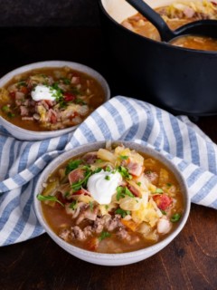 Sausage and cabbage stew in two bowls with a pot of soup in the background