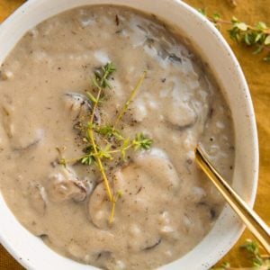 Dairy-Free Cream of Mushroom Soup in a oval ceramic bowl with fresh thyme sprinkled on top and a golden spoon to the side.