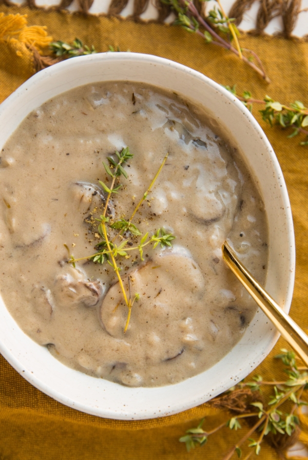 Dairy-Free Cream of Mushroom Soup in a oval ceramic bowl with fresh thyme sprinkled on top and a golden spoon to the side.