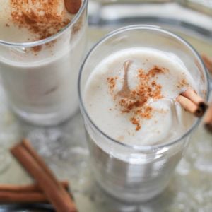 Naturally Sweetened and Dairy Free Horchata in two glasses with cinnamon sticks in the glasses and ice cubes. Sitting on a tray, ready to serve.