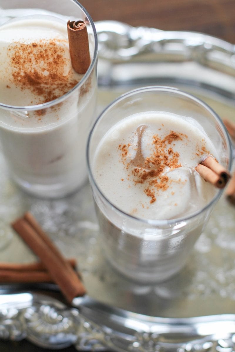 Naturally Sweetened and Dairy Free Horchata in two glasses with cinnamon sticks in the glasses and ice cubes. Sitting on a tray, ready to serve.