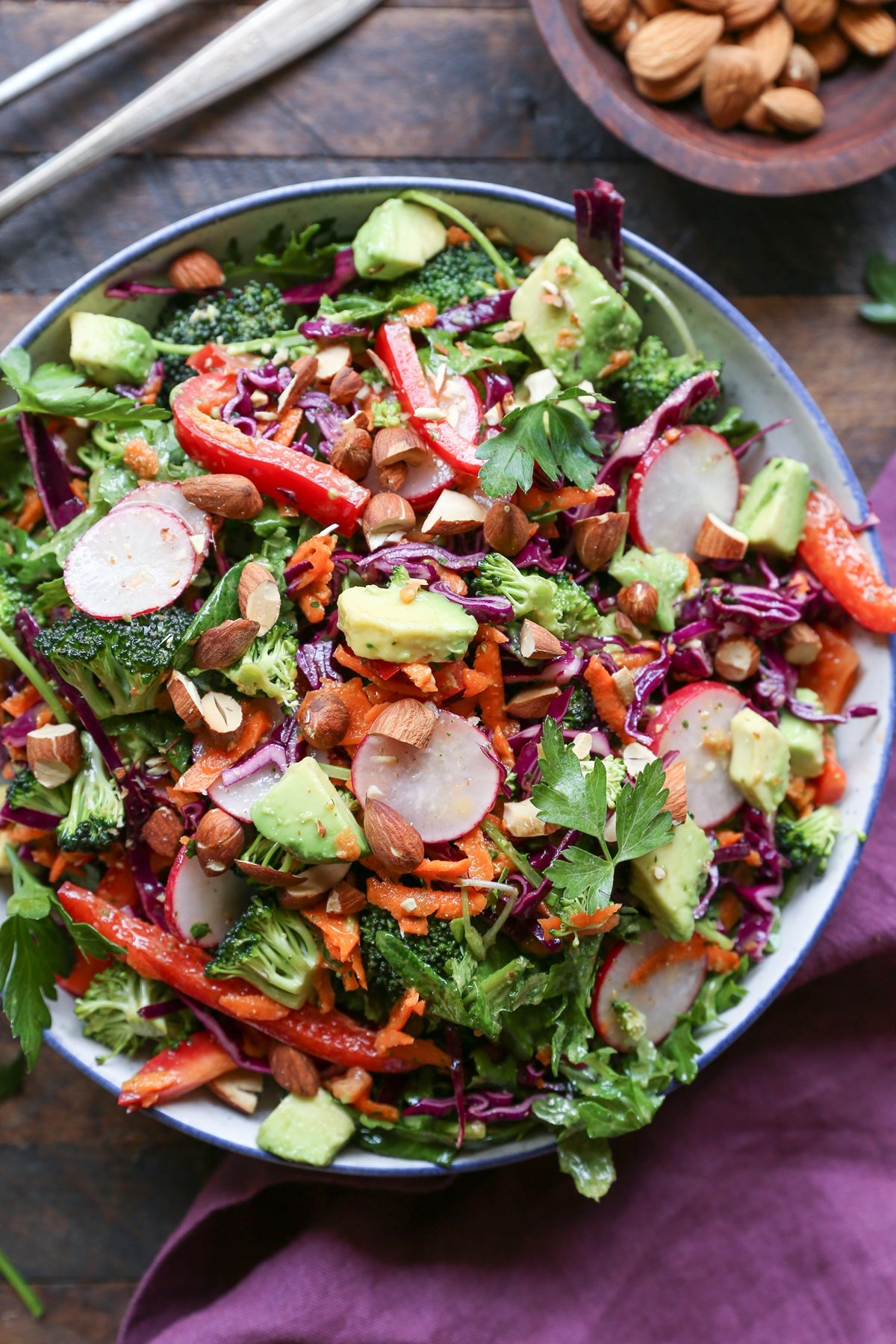 Big bowl of salad with vegetables, avocado, and nuts. Purple napkin to the side.