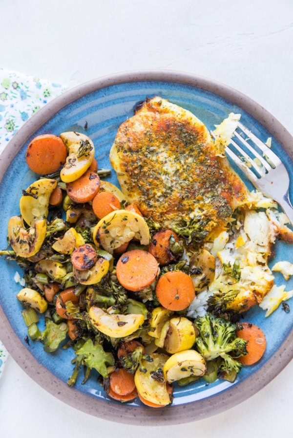 Easy Baked Cod Recipe with turmeric and paprika on a blue plate with roasted vegetables.