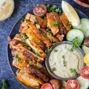 Plate of chicken shawarma with sauce and fresh vegetables to the side.